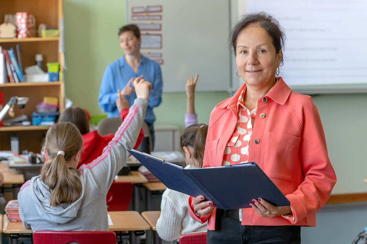 Schulleiterin Frau Heining steht in einer Schulklasse, im Hintergrund steht die Lehrerin an der Tafel und hält Unterricht